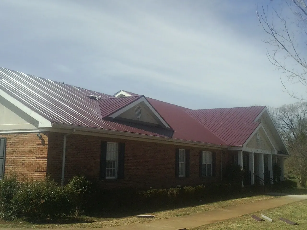 Red metal roof with gabled entries on a long brick building, from a Hail Damage Roof Repair job in Manhattan Beach