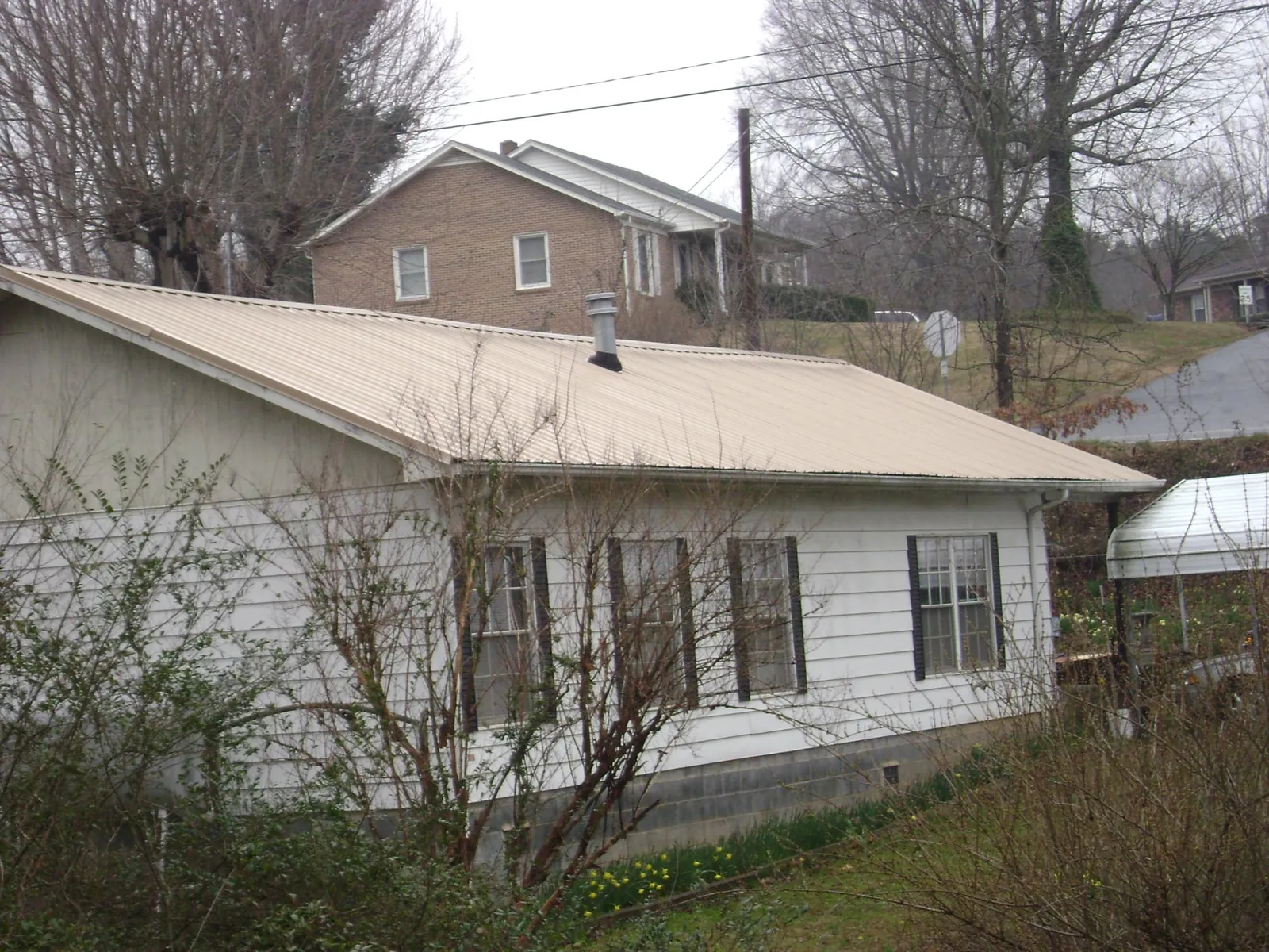 Tan metal roof on a white sided house set into a hillside — Commercial Roofing by Roofing Brothers in Manhattan Beach